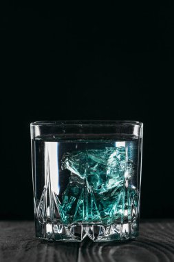 Siyah arka planda, tahta yüzeyinde mavi buz küpleri olan bir bardakta cin. Buzlu alkol..