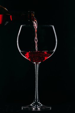 Şişeden çıkan kırmızı şarapla dolu bir bardak. Siyah arka planda şarap kadehi.