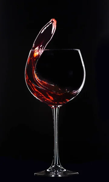 Large glass with red wine on a black background. Splashes of wine.