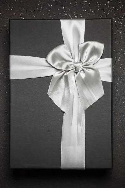 Black gift box with a silver ribbon and a large bow on a granite dark background.
