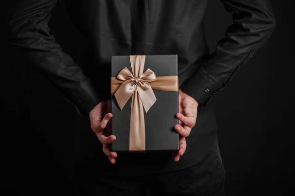 Hombre Con Una Camisa Negra Sostiene Regalo Con Una Cinta —  Fotos de Stock