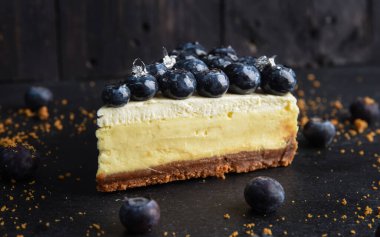 Tahta arka planda yaban mersinli cheesecake dilimi. Yukarıdan gelen dutlarla süslenmiş bir turta..