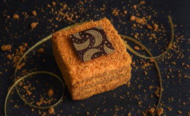 Yıldız ve ay desenli kare bir çikolatayla süslenmiş kare bir ballı pasta. Tahta bir arka planda turta.