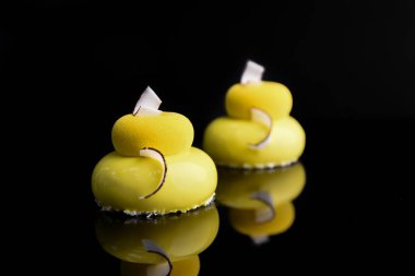 Yuvarlak pasta sarı jöleli ve siyah arka planda hindistan cevizi parçalarıyla süslenmiş..