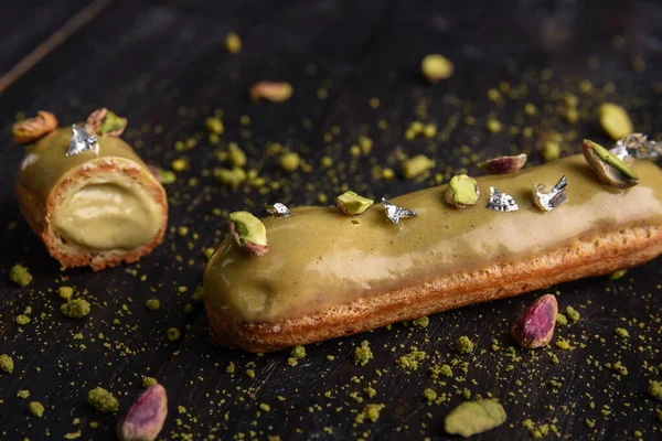 Üzerinde şam fıstığı parçaları ve koyu ahşap bir arka planda yenilebilir folyo bulunan cam kaplama. Ev yapımı tatlılar. Kesikte, dolgusu akan bir eklem..