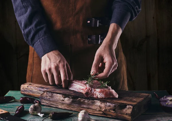 앞치마를 사람은 스테이크 로즈마리 가지를 놓는다 위에서 고기를 로열티 프리 스톡 이미지