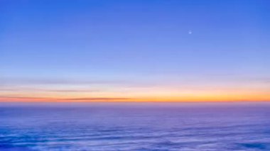 Denizin üzerinde büyüleyici renkli bir gün batımı. Hilal şeklinde küçük bir ay hüzünlü gökyüzünde hareket ediyor. Ay ışığı ve ilk alacakaranlık yıldızları ile huzurlu bir manzara için huşu dolu doğal bir manzara.
