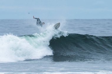 Bir sörfçü, Şili 'nin Puertecillo bölgesindeki Pasifik Okyanusu' nda büyük bir dalgaya binip düşüyor. Bulutlu bir havada vahşi bir manzarada sörf yapmak için inanılmaz dalgalar.