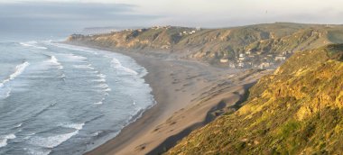 Okyanustan gelen dalgaların sahildeki kumu parçaladığı huzurlu bir sahil manzarası. Doğayla bağlantı kurmak için harika bir yer. Kayalıkların altındaki kumların içinde vahşi bir yer.