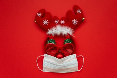 Kırmızı arka planda yüz maskesi ve süslemelerden yapılmış Noel geyikleri. Düz yatıyordu. Noel veya Yeni Yıl Kutlama Konsepti