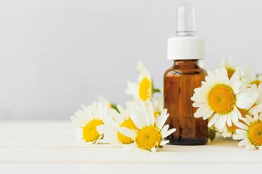 Papatya çiçekleri ve beyaz ahşap arka planda gerekli yağı içeren kozmetik şişeler. Boşluğu kopyala