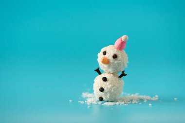 Mavi arka planda Noel Baba şapkalı hindistan cevizi toplarından yapılmış bir kardan adam. Yumuşak odaklanma. Noel kutlaması kavramı