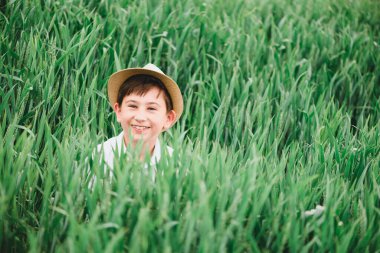 Gökyüzüne karşı yeşil çimlerin üzerinde gülümseyen mutlu çocuğun portresi. Yumuşak odaklanma. Yaz etkinlikleri