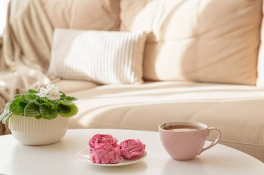 Pembe çiçek şekerlemeleri ve sehpada sıcak kanepeli çay. Yumuşak odak