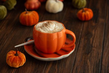 Balkabağı şeklinde bir kupada, sonbahar dekoruyla çevrili, krema ve baharatlı, kabak şeklinde bir latte.