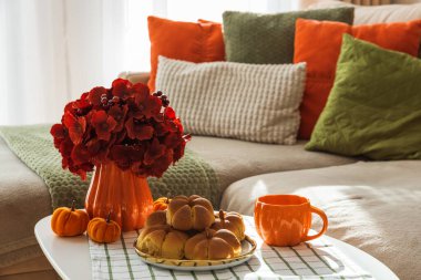 Kanepeli, yastıklı ve kahve masasında balkabaklı tarçınlı çöreklerle sonbahar oturma odası. 