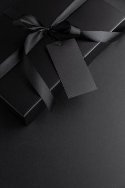Saten kurdeleli Kara Hediye Kutusu ve Karanlık Arkaplanda Boş Etiket