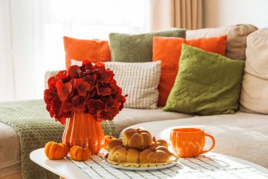 Kanepeli, yastıklı ve kahve masasında balkabaklı tarçınlı çöreklerle sonbahar oturma odası. 