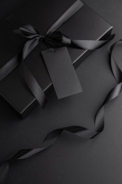 Saten kurdeleli Kara Hediye Kutusu ve Karanlık Arkaplanda Boş Etiket