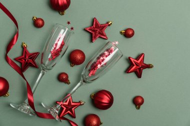 Şampanya flütleri ve Yeşil Arkaplanda Kırmızı Noel süsleri. Mutlu yıllar ya da Noel kutlamaları