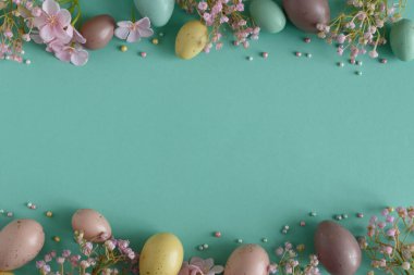 Pastel Easter Eggs and Flowers on Teal Background. Festive Spring Flatlay