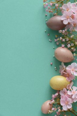 Pastel Easter Eggs and Flowers on Teal Background. Festive Spring Flatlay