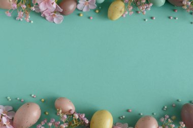 Pastel Easter Eggs and Flowers on Teal Background. Festive Spring Flatlay