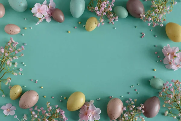 Pastel Easter Eggs and Flowers on Teal Background. Festive Spring Flatlay