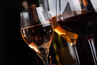 Üç bardak kırmızı, beyaz ve ışıl ışıl gül şarabı. Arka plandaki şişelere karşı koyu renkli bir demet üzümle birlikte.