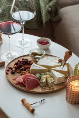 Çeşitli peynirler, kurutulmuş etler, cevizler, kuru kızılcıklar, ekmek çubukları, zeytin ve kırmızı jöle içeren zarif şarküteri kompozisyonu, iki kadeh kırmızı şarapla eşleştirildi.