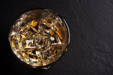 Kahverengi viski ve buz küpleriyle dolu çarpık tasarım camları, yakınlarda eriyen buzlarla birlikte koyu bir yüzeye yerleştiriliyor.