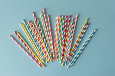 Açık mavi arkaplanda fan benzeri desenlerde düzenlenmiş çevre dostu renkli çizgili kağıt pipetler.