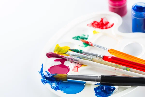 Pinturas coloridas sobre paleta y pinceles sobre fondo blanco — Foto de Stock