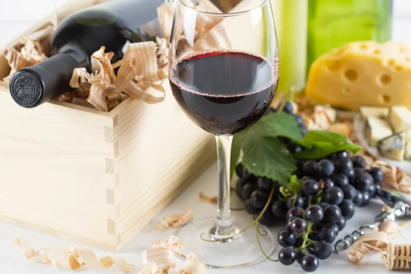 Sklenice červeného vína a hroznů, sýr a víno láhev na bílém — Stock fotografie