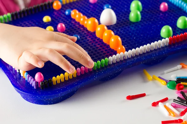 As mãos da criança para construir um mosaico de plástico pino multicolorido — Fotografia de Stock