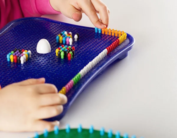 As mãos da criança para construir um mosaico de plástico pino multicolorido — Fotografia de Stock