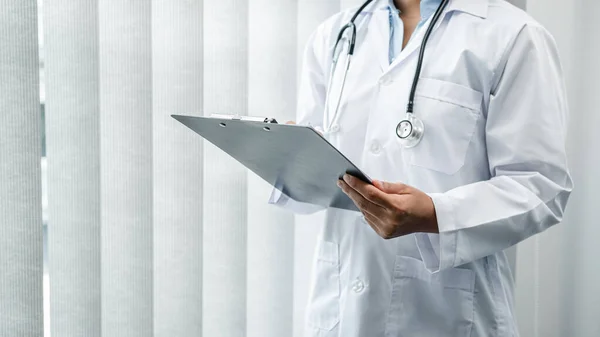 The doctor is standing and reading medical report inside his office, the doctor is reading the patient\'s symptoms and analyze treatment, Health care and medicine used to treat the patient
