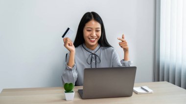 Genç Asyalı bir kadın online alışveriş için dizüstü bilgisayar kullanıyor ve online ödeme siparişi için kredi kartı bilgilerini tutuyor.