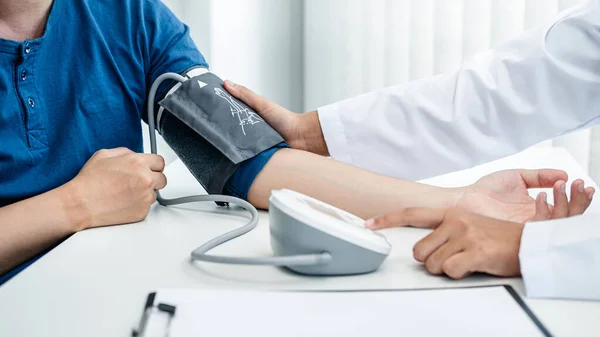 Doctor is checking the patient blood pressure in his hospital office, and doctor is pressing a button, an instrument used for measuring blood pressure on the table
