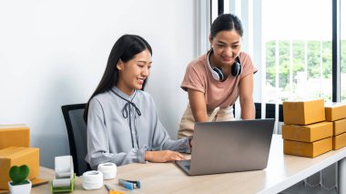 İki genç iş kadını dizüstü bilgisayarla siparişleri kontrol ediyor ve müşteriyle konuşurken gülümsüyor. Kuryeler paket paketlerini eve teslim etmek için hazırlıyorlar.