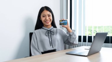 Genç Asyalı kadın gülümsüyor ve elinde kredi kartı ile online alışveriş için ödeme yaptığına dair güvenini gösteriyor.