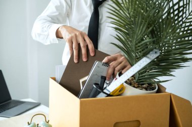 İş adamı çalışanı not defteri topluyor ve işten istifa ettiğinde ya da iş değiştirdiğinde iş yerinden ayrılmak için kişisel eşyalarını kahverengi karton kutuya koyuyor.