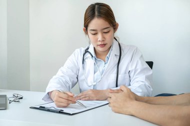 Doktor, klinikte hastaya reçete yazmadan ve tedavi tavsiyesi vermeden önce hastalık ve hastalık belirtilerini açıklayan bir belgeye işaret ediyor.