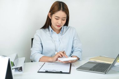 Kadın ofis çalışanı yeni bir iş projesinin kârını hesaplamak için hesap makinesine basıyor ve işini iyi yaptığında mutlu oluyor.