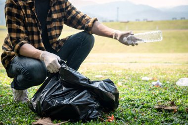 Eldivenli gönüllü bir adam plastik şişeyi plastik poşete koyup çöpleri toplamak için çevresel aktivite sırasında parkı temizliyor.