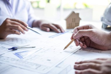 İnşaat mühendisliği ekibi veya mimar ortağı bir planı tartışırken, mimari proje için çizim ve çizim toplantısının bilgilerini mühendislik teçhizatı aracıyla kontrol ederler..