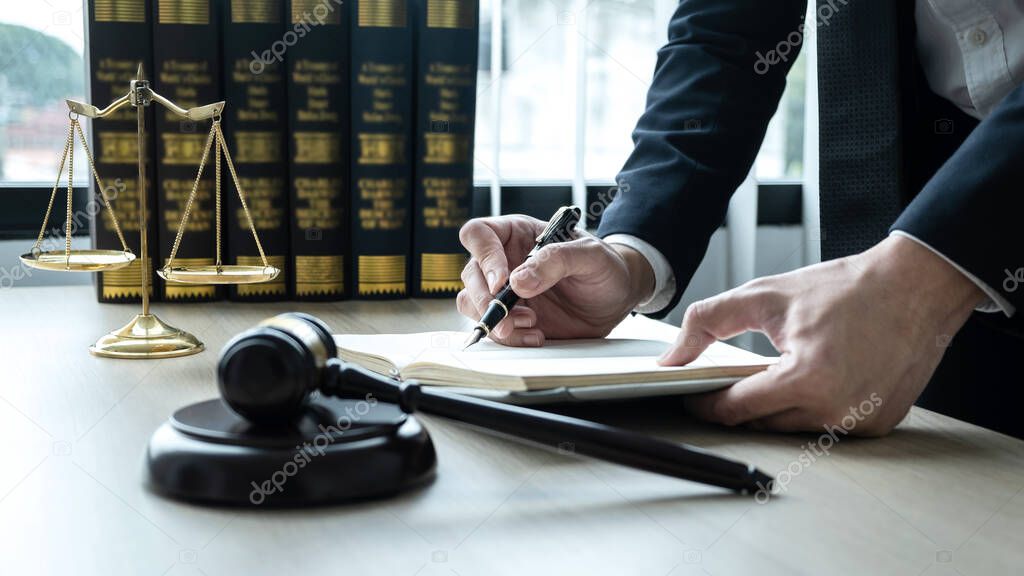 Counselor lawyer or notary working on a documents and report of the important case and wooden gavel, brass scale on table in courtroom.