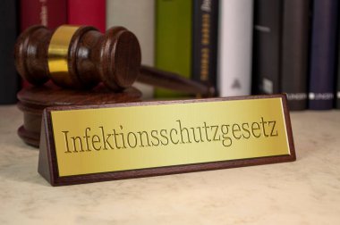 Tokmak ve hukuk kitaplarının olduğu altın tabela ve enfeksiyona karşı korunma yasasının Almanca karşılığı Infektionsschutzgesetz