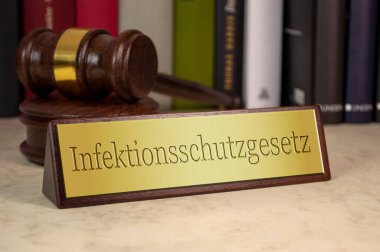 Golden sign with gavel and law books and the german word for Law on Protection against Infection - Infektionsschutzgesetz clipart