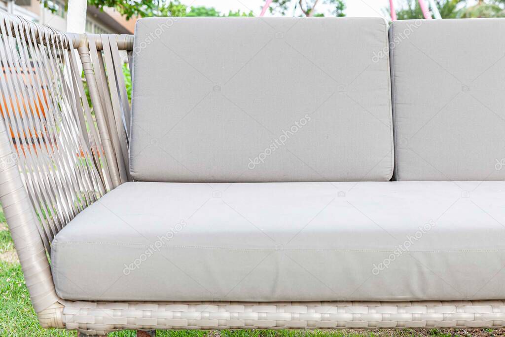 Long brown wicker sofa and white cushions and cushions placed on the lawn